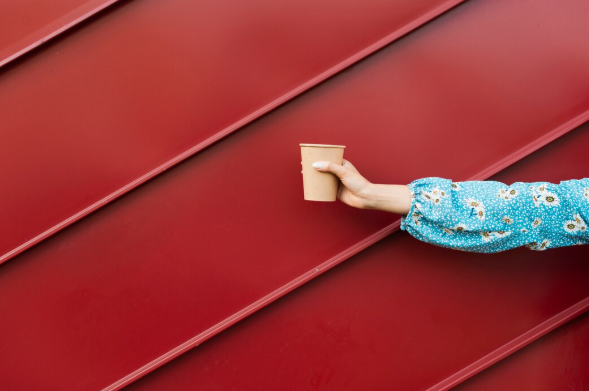 Hand holding coffee cup in front of a roof